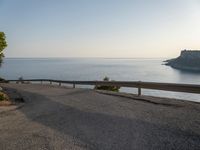 a road in front of a cliff overlooking the water and coastline with a bench next to it