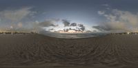 a fisheye lens photo of a sunset on a beach in a circle that has tracks from sand to water