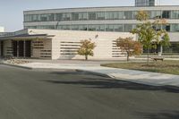 an empty street near a very large building with cars parked along it in front of it