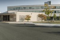 an empty street near a very large building with cars parked along it in front of it