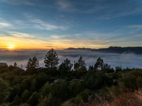 a sky view over a mountain surrounded by fog at sunset time with hills in the background