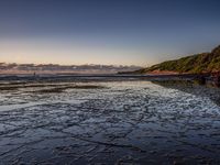 a sandy beach with sand and rocks at low tide with people in the distance walking on a sandy shoreline