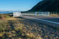 a highway going along the side of a grassy hill with a fence on it in a remote area