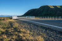 a highway going along the side of a grassy hill with a fence on it in a remote area