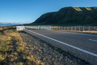 a highway going along the side of a grassy hill with a fence on it in a remote area