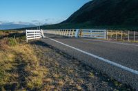 a highway going along the side of a grassy hill with a fence on it in a remote area