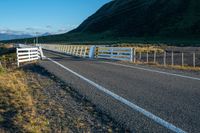 a highway going along the side of a grassy hill with a fence on it in a remote area