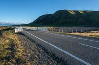 a highway going along the side of a grassy hill with a fence on it in a remote area