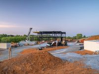 a picture of a building being built on a field near a forest in the background