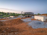 a picture of a building being built on a field near a forest in the background