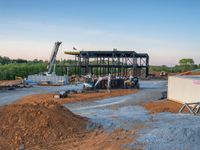 a picture of a building being built on a field near a forest in the background