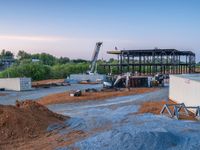 a picture of a building being built on a field near a forest in the background