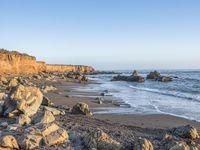 a grassy field by the shore and a cliff with rocks in the ocean in the background