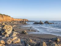 a grassy field by the shore and a cliff with rocks in the ocean in the background