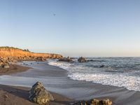 a grassy field by the shore and a cliff with rocks in the ocean in the background