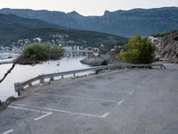 the view of a body of water with mountains in the background and parked cars parked next to the fence