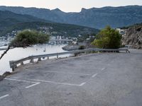 the view of a body of water with mountains in the background and parked cars parked next to the fence