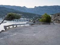 the view of a body of water with mountains in the background and parked cars parked next to the fence