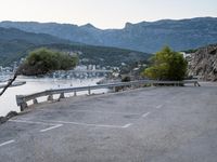 the view of a body of water with mountains in the background and parked cars parked next to the fence