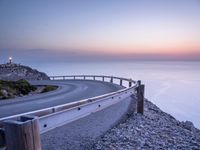 winding road along the coast at sunset, near ocean shore and distant lights in distance