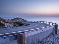 winding road along the coast at sunset, near ocean shore and distant lights in distance