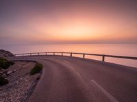 a empty road stretching towards the ocean with a sunset behind it that is very pretty