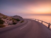 a empty road stretching towards the ocean with a sunset behind it that is very pretty