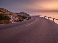 a empty road stretching towards the ocean with a sunset behind it that is very pretty