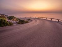 a empty road stretching towards the ocean with a sunset behind it that is very pretty