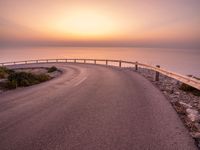 a empty road stretching towards the ocean with a sunset behind it that is very pretty