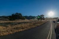 the sun shines over a car driving through the country side of the road while it's been on the road