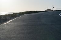 an empty road near a beach and waves as well as cars on the sand and houses on the beach