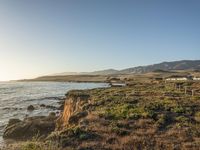 a grassy field by the shore and a cliff with rocks in the ocean in the background