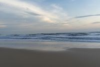 someone in the ocean at the beach watching the waves go by on the shore at sunset