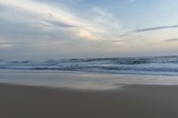 someone in the ocean at the beach watching the waves go by on the shore at sunset