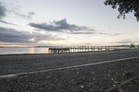 a wooden pier and a paved walkway over the water at sunset near a beach area