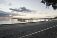 a wooden pier and a paved walkway over the water at sunset near a beach area