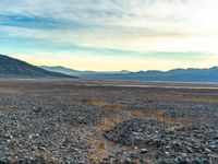 an open plain with rocks, grass and mountains behind it and blue sky in the background