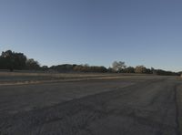 a person standing on a dirt road near a field with trees in the background under a clear sky