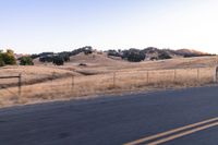 a motorcycle traveling along a rural road with hills in the background and a fence separating the middle