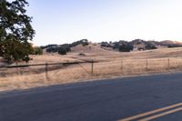 a motorcycle traveling along a rural road with hills in the background and a fence separating the middle