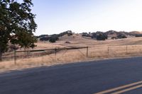 a motorcycle traveling along a rural road with hills in the background and a fence separating the middle