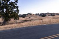 a motorcycle traveling along a rural road with hills in the background and a fence separating the middle