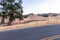 a motorcycle traveling along a rural road with hills in the background and a fence separating the middle