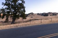 a motorcycle traveling along a rural road with hills in the background and a fence separating the middle