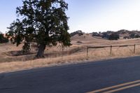 a motorcycle traveling along a rural road with hills in the background and a fence separating the middle