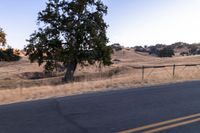 a motorcycle traveling along a rural road with hills in the background and a fence separating the middle