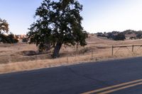 a motorcycle traveling along a rural road with hills in the background and a fence separating the middle