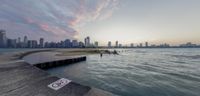 the sun is rising over the skyline at sunset near the water's edge in front of a large city