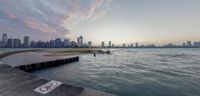 the sun is rising over the skyline at sunset near the water's edge in front of a large city